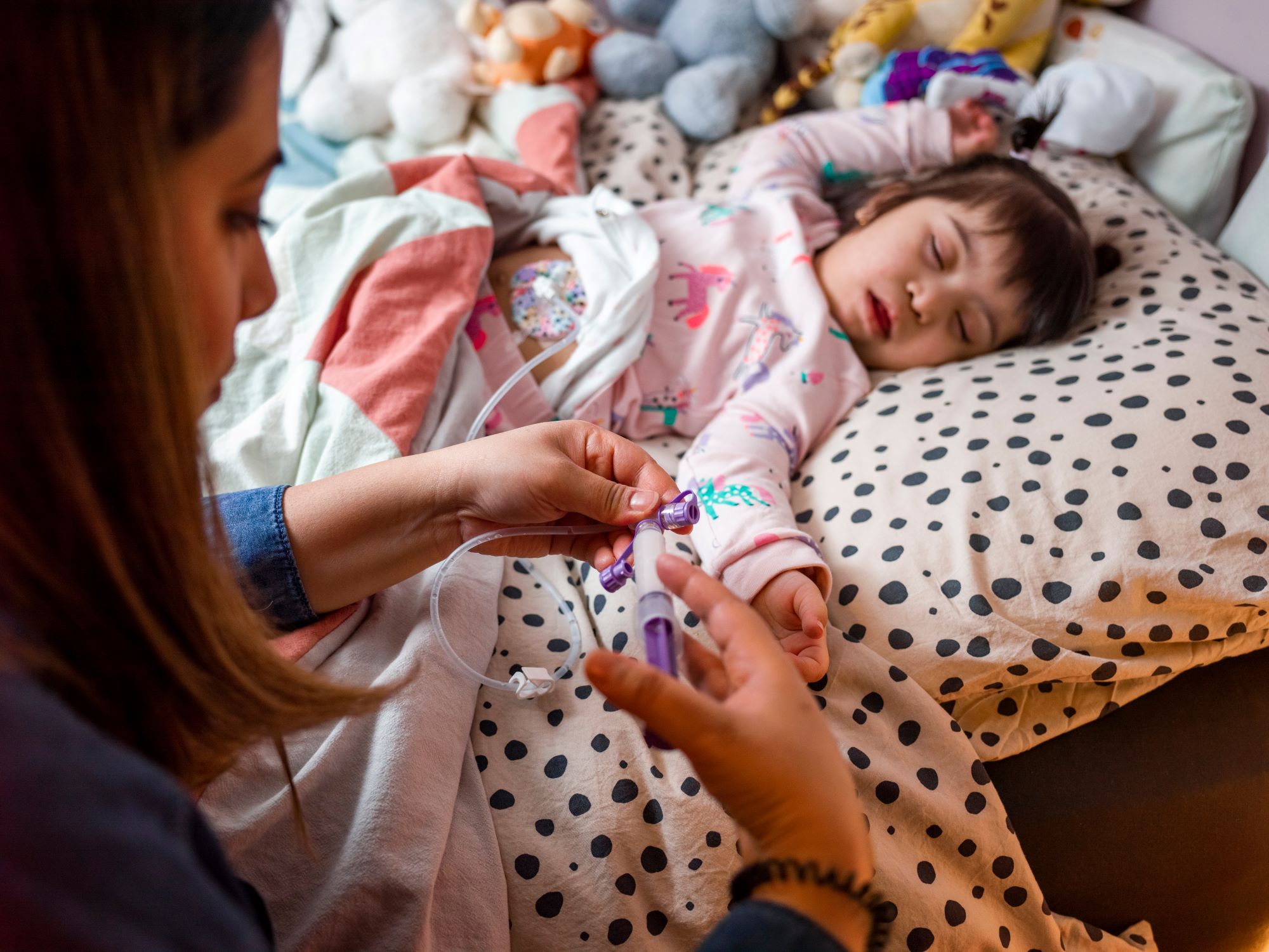 Mother at bedside of her sleeping disabled daughter who requires a feeding tube.